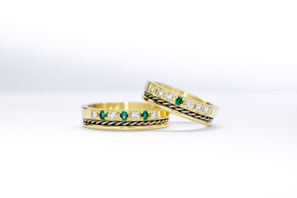 alianzas de oro 18k amarillo y blanco con diamantes y esmeraldas engarzadas sobre fondo blanco